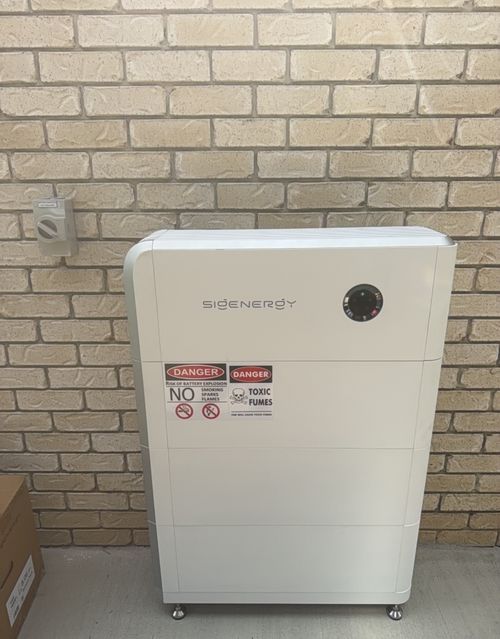 Sigenergy battery stack installed against a brick wall, with an isolator switch and battery safety signage