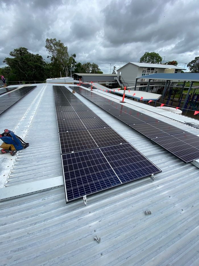Long rows of new solar panels being installed on a corrugated iron roof, with safety flags along the edge